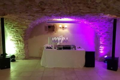 Table de DJ équipée de matériel audio, installée dans une salle voûtée en pierre avec éclairage coloré.