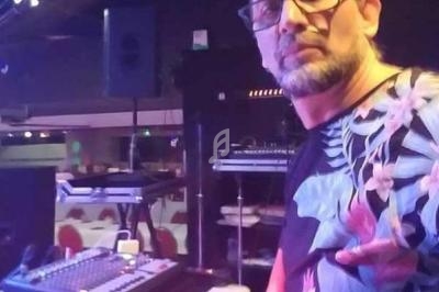 Homme devant une console de mixage dans une salle avec tables et chaises en arrière-plan.