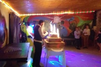 Un homme en costume allume des cierges magiques sur un gâteau à plusieurs étages dans une salle décorée et éclairée.