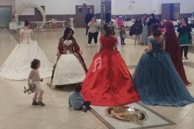 Des femmes en robes de soirée colorées discutent dans une grande salle, avec des enfants jouant au sol.