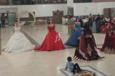 Des femmes en robes de cérémonie colorées dansent dans une grande salle, entourées de quelques spectateurs.