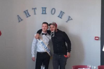 Deux hommes posent côte à côte dans une salle, l'un portant une écharpe ’Mister 2015’ et un nœud papillon.