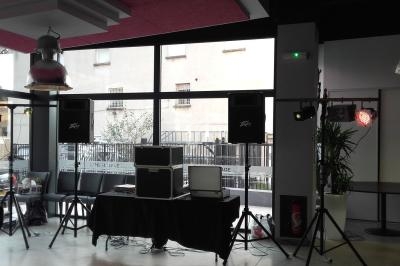 Installation de matériel audio et éclairage dans une salle avec grandes fenêtres donnant sur l'extérieur.