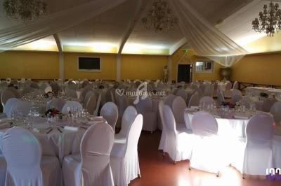 Salle de réception décorée avec des tables rondes, nappes blanches, chaises houssées et lustres suspendus.
