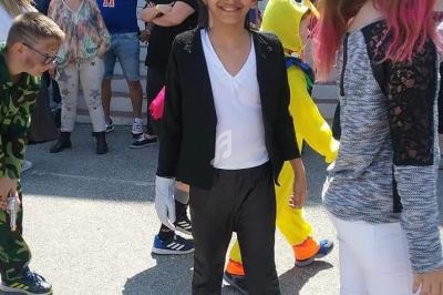 Un enfant déguisé en tenue noire et blanche, entouré d'autres personnes lors d'un événement en extérieur.