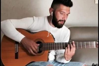 Un homme assis sur un canapé joue de la guitare acoustique tout en portant des écouteurs.