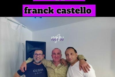 Trois hommes posant ensemble dans une pièce blanche, l'un au centre portant une chemise à motifs.