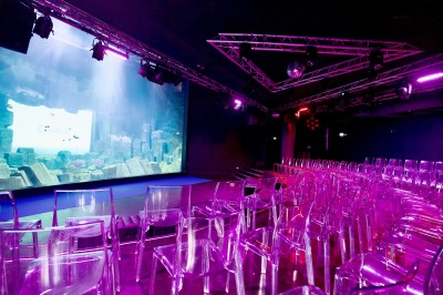 Tunnel d'aquarium avec un grand bassin à droite, éclairages colorés et écran lumineux sur le mur gauche.