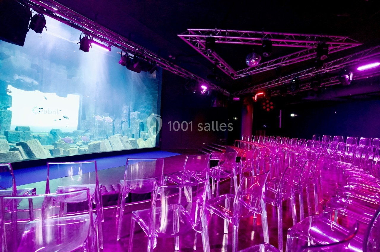 Salle de conférence avec des chaises transparentes et un écran géant affichant une scène sous-marine.