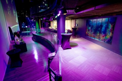 Tunnel d'aquarium avec un grand bassin à droite, éclairages colorés et écran lumineux sur le mur gauche.