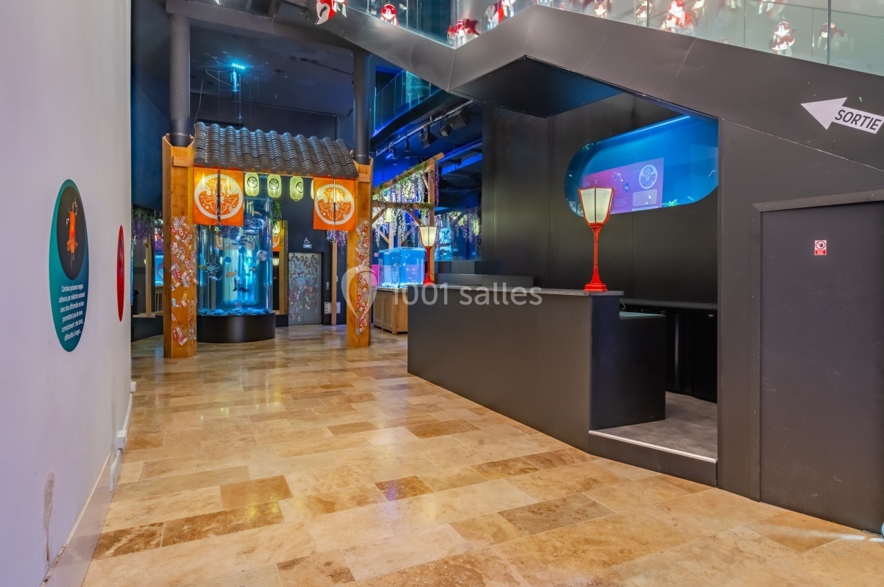 Couloir intérieur avec sol en marbre, décorations asiatiques, aquariums éclairés et panneau indiquant la sortie.