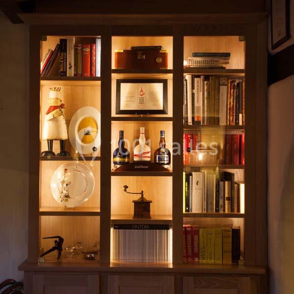 Bibliothèque éclairée avec des étagères contenant des livres, des bouteilles, des objets décoratifs et des cadres.