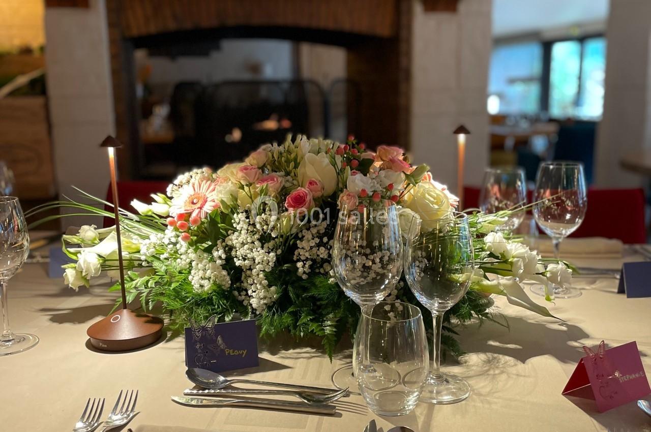 Table élégamment dressée avec un centre de table floral, des verres à vin et des couverts, devant une cheminée.