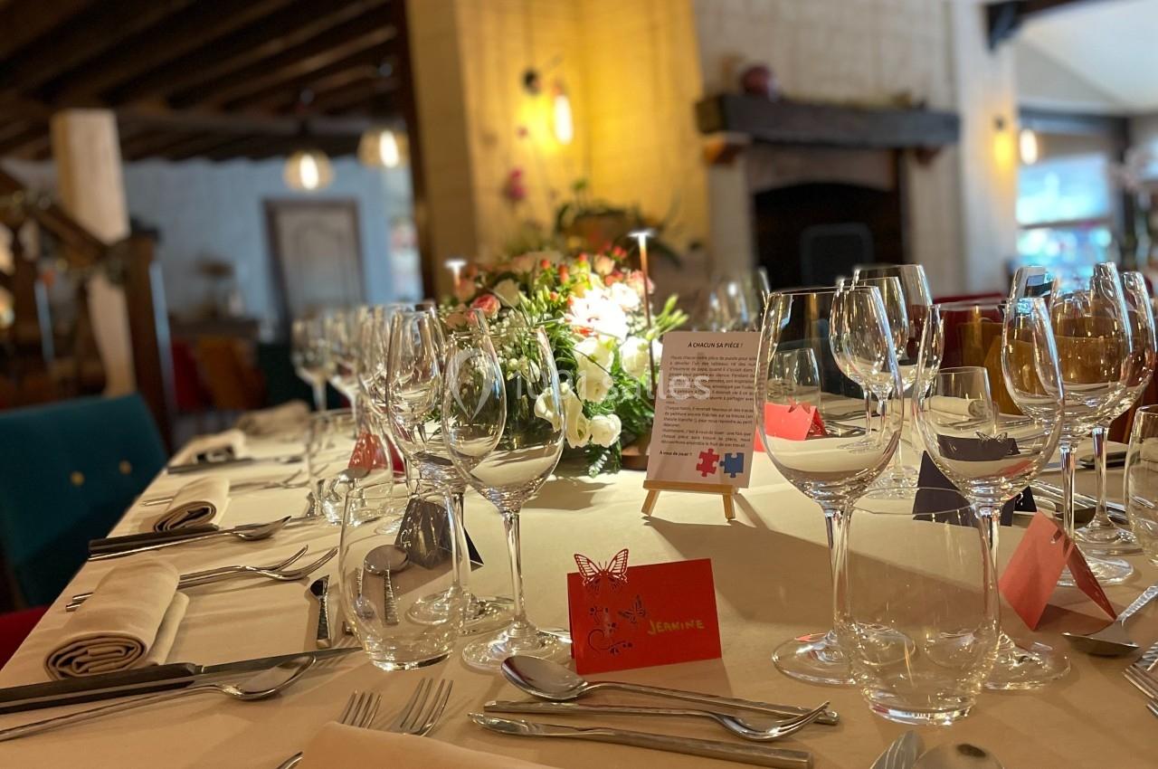 Table élégamment dressée avec des verres, couverts et décorations florales dans un restaurant à l'ambiance chaleureuse.
