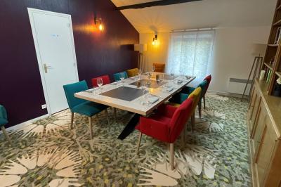 Table dressée avec des verres, couverts et serviettes, entourée de chaises colorées dans une salle lumineuse avec…