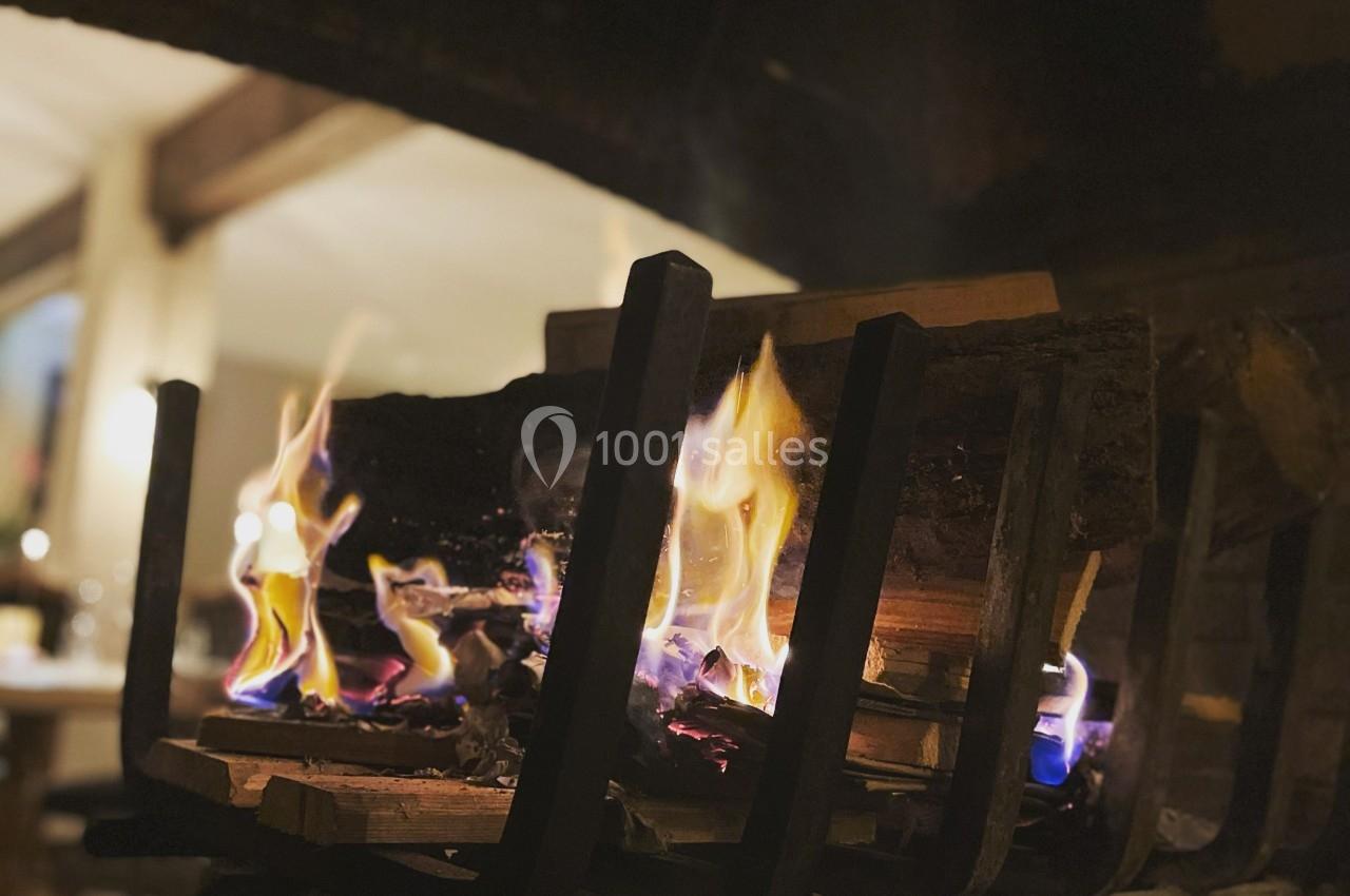Bûches enflammées dans un foyer ouvert, éclairant un intérieur chaleureux avec des tables en arrière-plan.