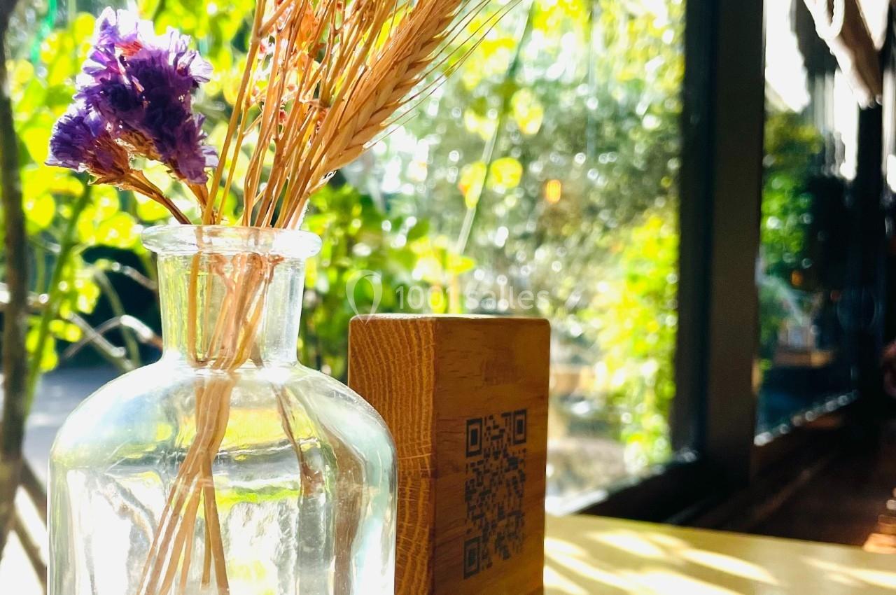 Petit vase en verre contenant des fleurs séchées, posé sur une table en bois près d'une fenêtre lumineuse.