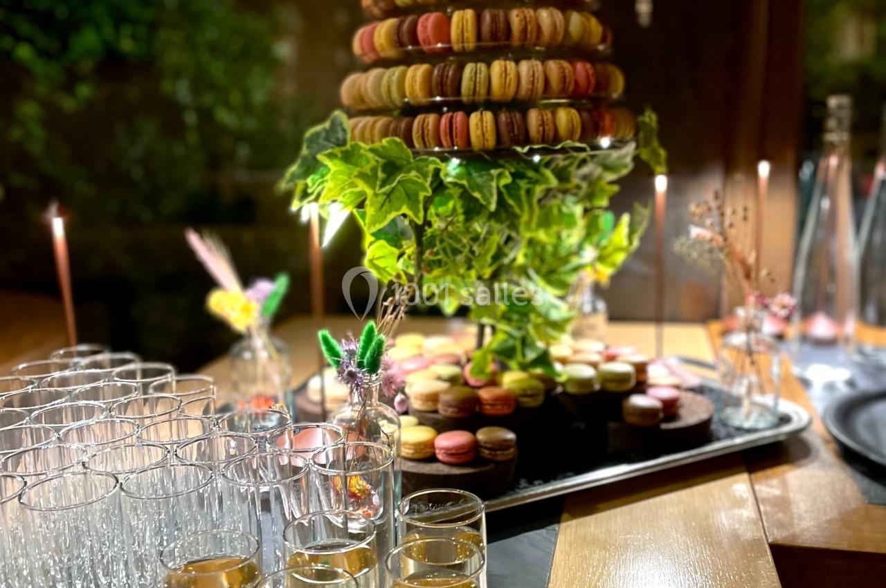 Tour de macarons colorés sur un plateau décoré de verdure, entourée de flûtes de champagne sur une table en bois.