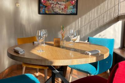 Table dressée avec des verres, couverts et serviettes, entourée de chaises colorées dans une salle lumineuse avec…