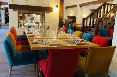 Table dressée avec des verres, couverts et serviettes, entourée de chaises colorées dans une salle lumineuse avec…