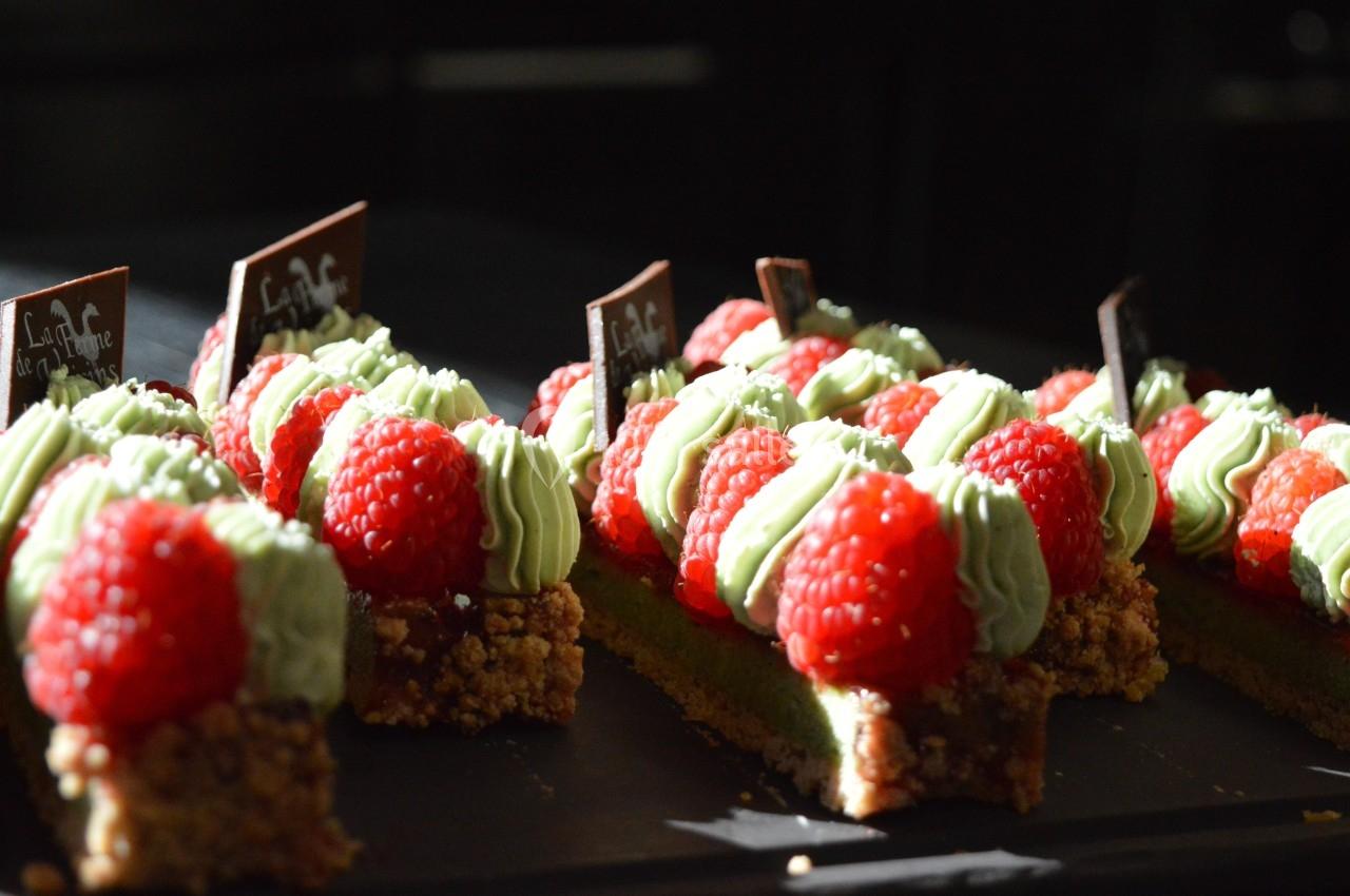 Gâteaux individuels décorés de framboises fraîches et de crème verte, posés sur un plateau sombre.
