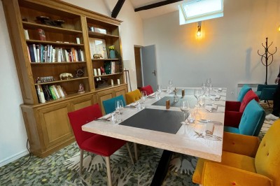 Table dressée avec des verres, couverts et serviettes, entourée de chaises colorées dans une salle lumineuse avec…