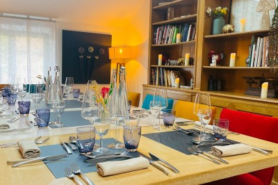 Table dressée avec des verres, couverts et serviettes, entourée de chaises colorées dans une salle lumineuse avec…
