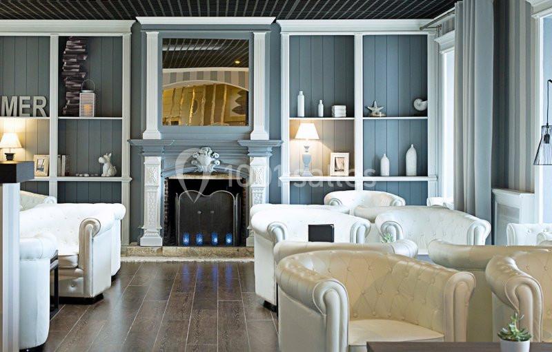 Salon élégant avec fauteuils capitonnés blancs, cheminée décorative et étagères murales garnies d'objets.