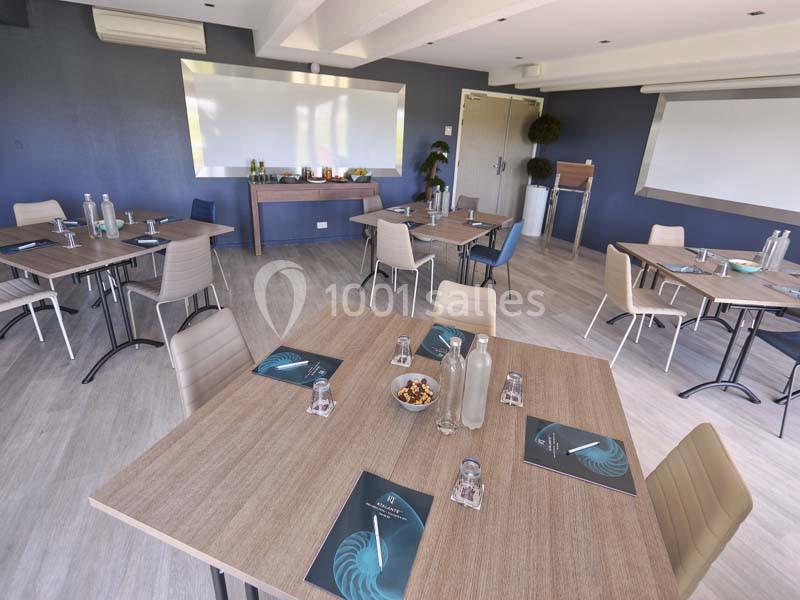 Salle de réunion lumineuse avec tables en bois, chaises modernes, tableau blanc et matériel de conférence.