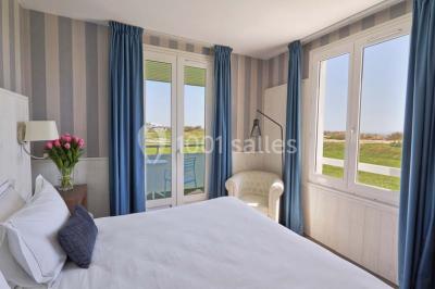 Vue aérienne d'un bâtiment en bord de mer entouré de champs et de vignobles sous un ciel dégagé.