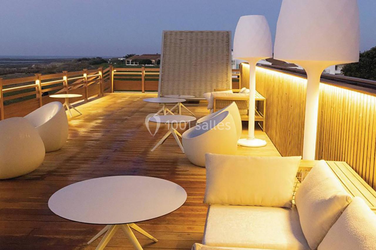 Terrasse en bois avec mobilier moderne, éclairage doux et vue dégagée sur un paysage au crépuscule.