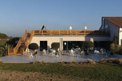 Vue aérienne d'un bâtiment en bord de mer entouré de champs et de vignobles sous un ciel dégagé.