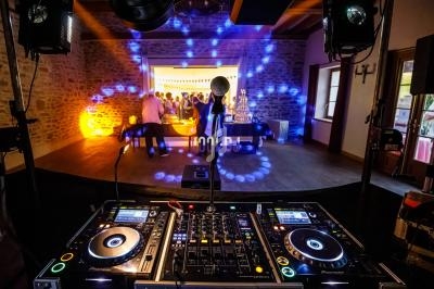 Vue depuis une table de mixage de DJ avec une piste de danse éclairée et des invités en arrière-plan.