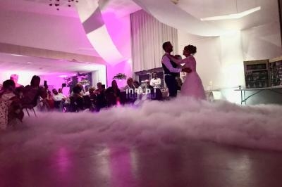 Un couple danse au milieu d'une piste enveloppée de fumée, sous un éclairage rose dans une salle de réception.