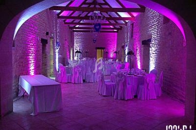 Salle de réception en pierre avec tables dressées et éclairage violet, ambiance festive et élégante.