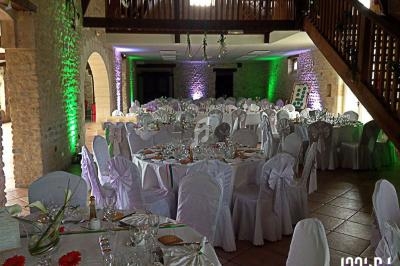 Salle de réception décorée avec des tables rondes dressées, nappes blanches et éclairage coloré sur les murs en pierre.