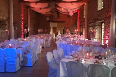 Salle de réception décorée pour un mariage, avec tables dressées, chaises couvertes et éclairage tamisé.