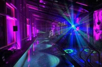 Piscine intérieure éclairée par des lumières colorées et des effets lumineux dans une ambiance nocturne.