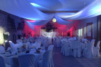 Salle de réception décorée avec des nappes blanches, des éclairages colorés et des tables rondes dressées.