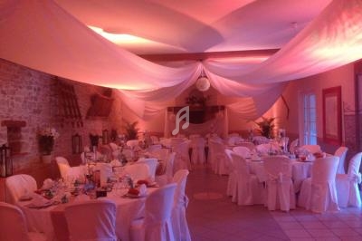 Salle de réception décorée avec des nappes blanches, des tables dressées et un éclairage tamisé.