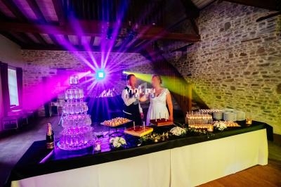 Table de réception décorée avec des desserts, une fontaine de champagne et des jeux de lumière colorés dans une salle en…