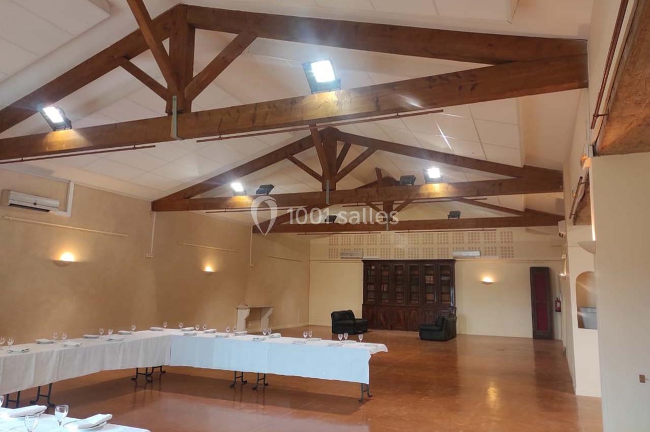 Salle spacieuse avec poutres apparentes, tables dressées pour un événement et éclairage au plafond.