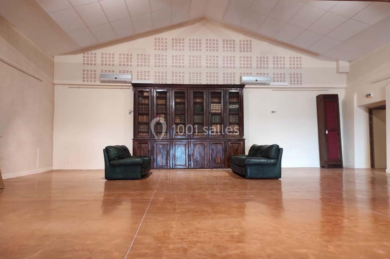Salle spacieuse avec sol en béton, deux canapés verts face à une bibliothèque en bois sombre.