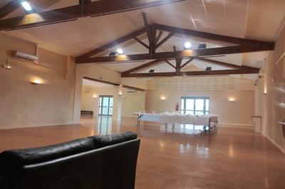 Un jardin verdoyant avec pelouse, arbustes, olivier central et allées bordées de végétation sous un ciel dégagé.