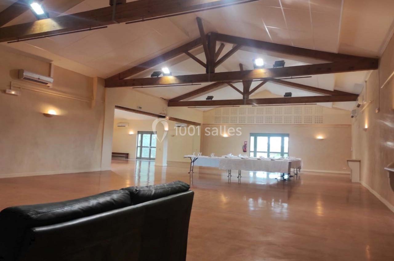 Salle spacieuse avec poutres apparentes, tables dressées au fond et canapé au premier plan.