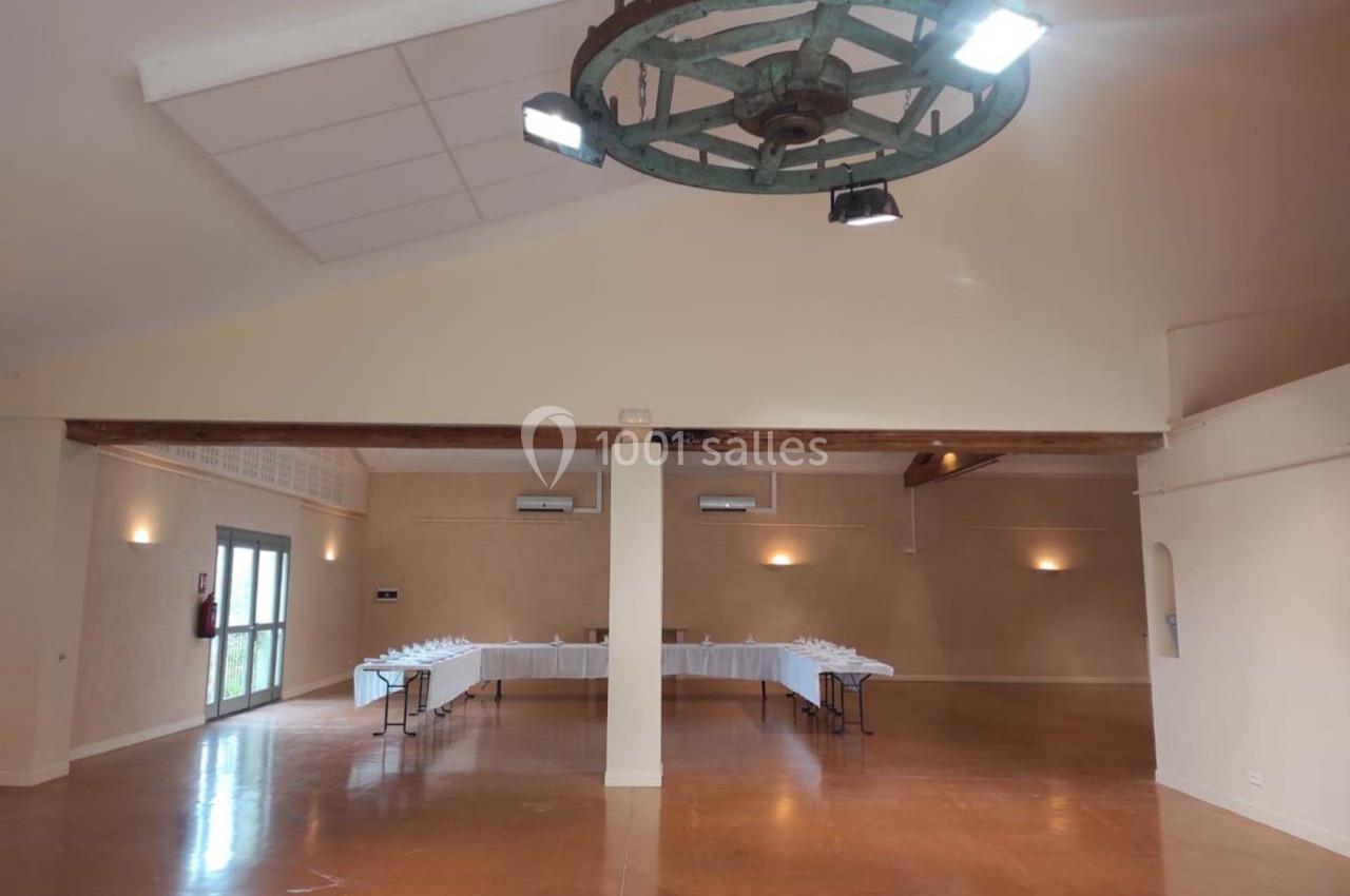 Salle spacieuse avec un sol en béton ciré, une grande table dressée au fond et un lustre en bois suspendu au plafond.