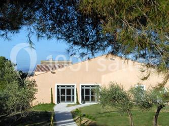 Bâtiment beige avec toit en tuiles, entouré d'arbres et d'un chemin en gravier menant à l'entrée.