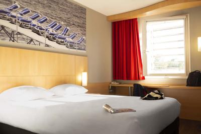 Chambre d'hôtel lumineuse avec un lit double, une fenêtre avec rideaux rouges et un bureau en bois clair.
