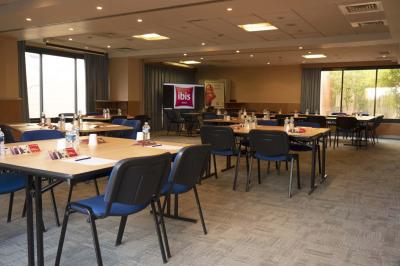 Chambre d'hôtel lumineuse avec un lit double, une fenêtre avec rideaux rouges et un bureau en bois clair.