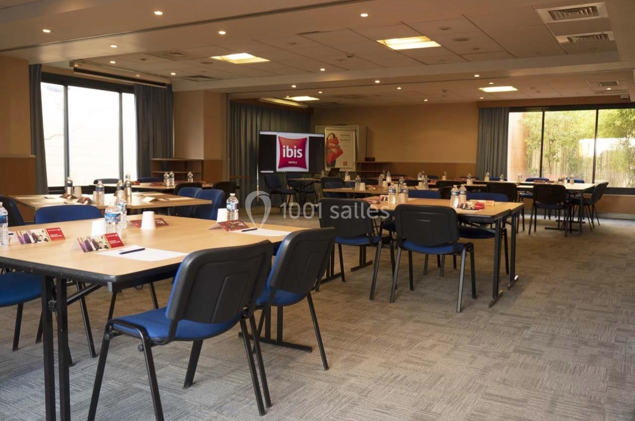 Salle de réunion lumineuse avec tables disposées en U, chaises bleues et matériel de conférence.